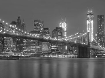 Black and white night view of Brooklyn Bridge with city lights.