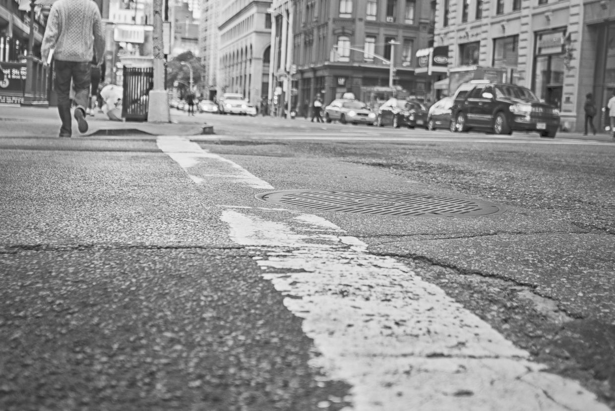 Street view focusing on a manhole and urban crosswalk lines.