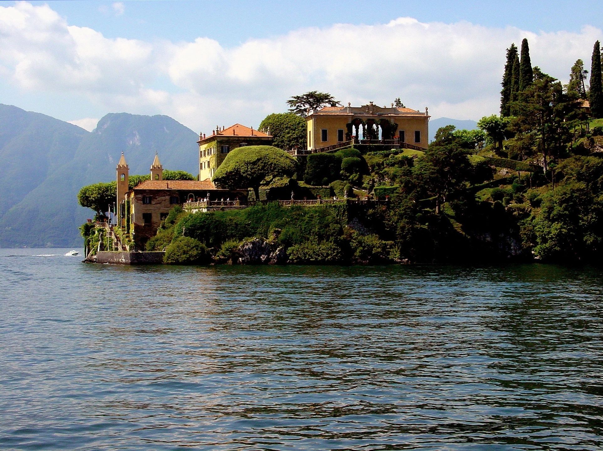 Scenic villa on a lush lakeside peninsula with mountains in the background.