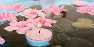 Pink flowers and a lit candle floating on water with smooth stones.