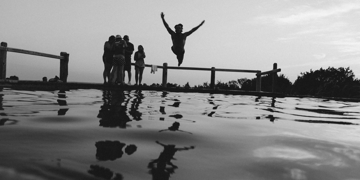 Person jumping into water while others watch on the dock.