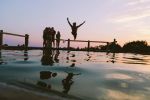 A person jumps excitedly into a lake at sunset with friends nearby.