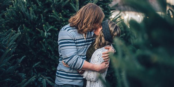 Couple sharing a kiss among pine trees.