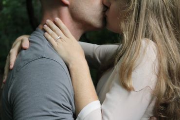 A couple sharing a tender kiss with an engagement ring visible.