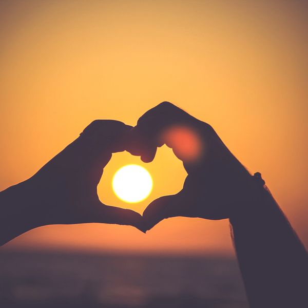 Hands forming a heart around the setting sun.