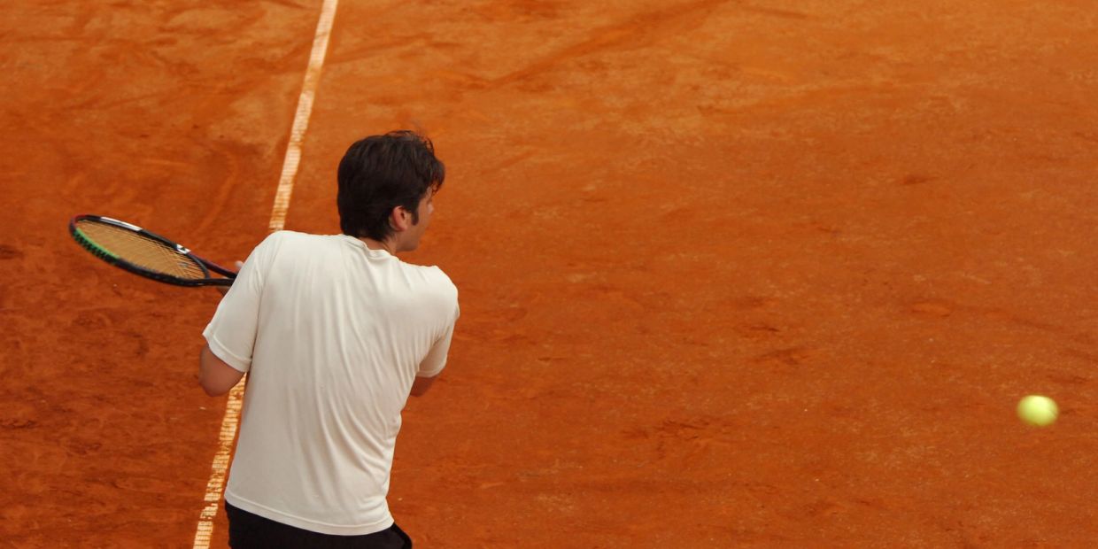 Tennis player in white shirt hitting a ball on a clay court.