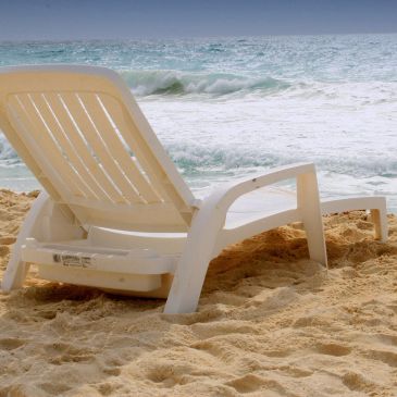 White lounge chair on sandy beach by ocean.