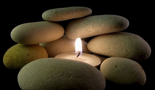 A candle surrounded by smooth stones on a black background.