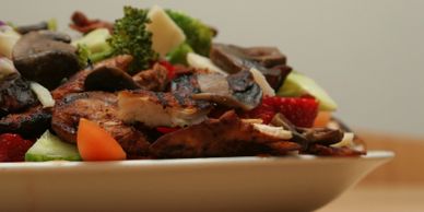 Plate of grilled chicken with mushrooms and fresh vegetables.