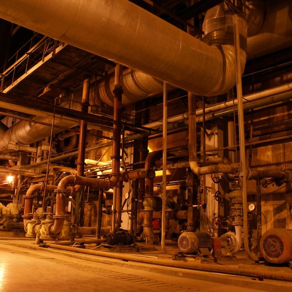 Industrial pipes and machinery inside a factory with warm lighting.