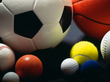 Various sports balls grouped together on a dark surface.