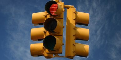 Yellow traffic light showing a red signal against a blue sky.