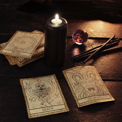 Tarot cards, a black candle, incense sticks, and a crystal ball on a dark surface.