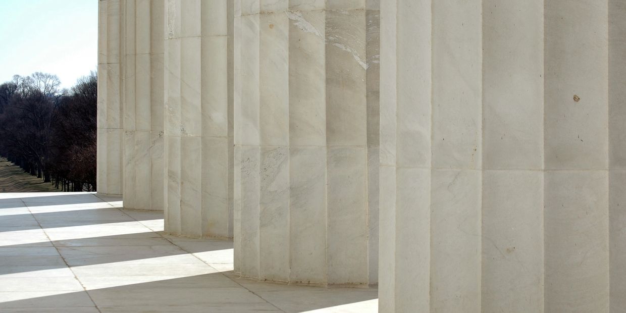 Close-up of large marble columns casting shadows on the ground.