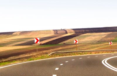 Curved road with directional signs through patchy farmland.
