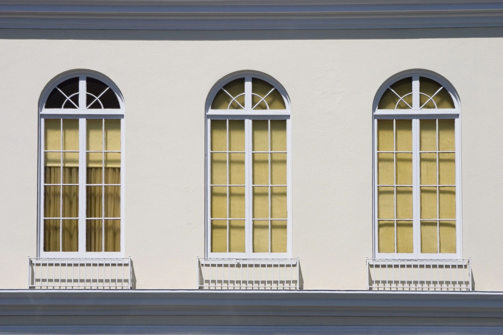 Three arched windows with yellow curtains and white railings.