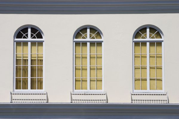 Three arched windows with yellow curtains on a white building facade.