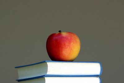 Red apple resting on two stacked books against a plain background.