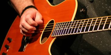 Hand strumming an acoustic guitar with focus on strings and sound hole.