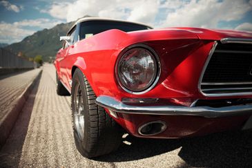 Close-up of a shiny red vintage car under a partly cloudy sky.