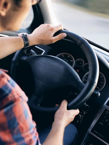 Man driving a car with hands on the steering wheel.