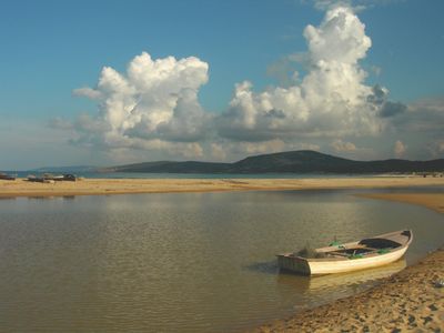 A lone boat rests on a calm shore under a sky with large fluffy clouds.