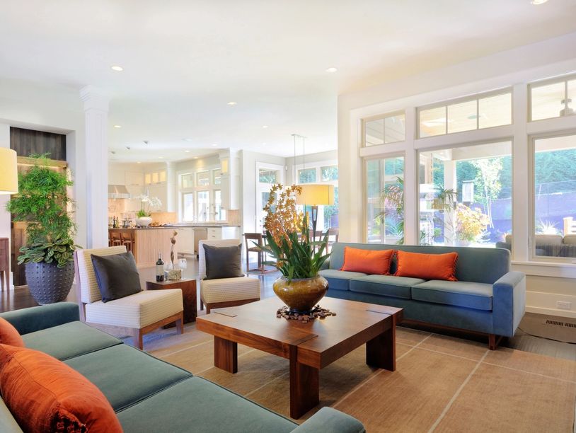 Bright living room with teal sofas and orange pillows around a wooden coffee table.