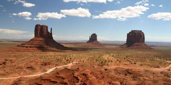 Desert with red sand, three stand alone mountains, and a sky with scattered clouds