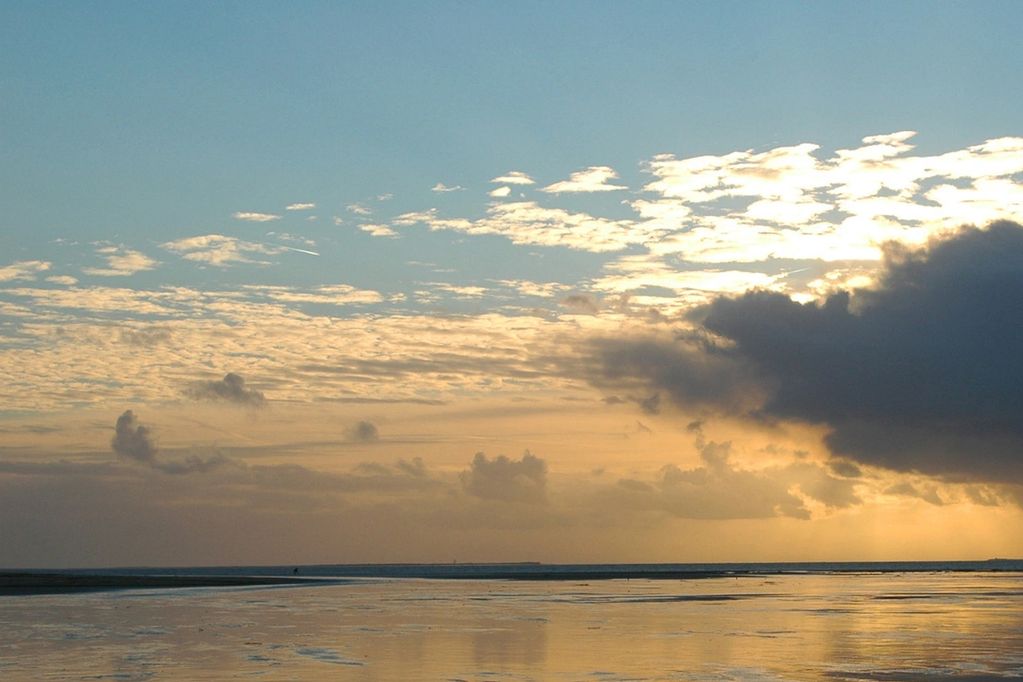 A serene sunset over calm water with dramatic clouds and reflections.
