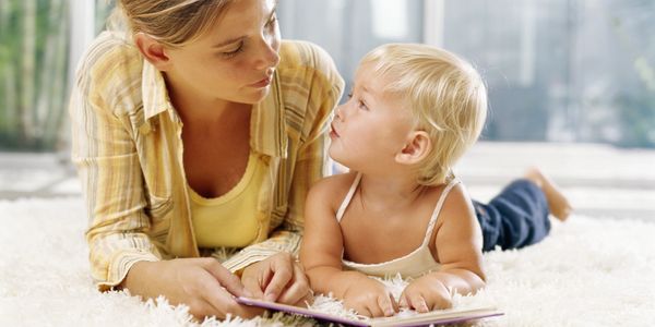 Mother and toddler reading a book together on the floor.