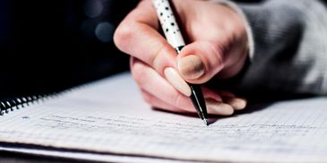 Close-up of a hand writing in a notebook with a pen.