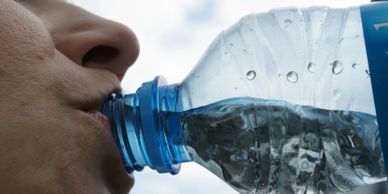 Close-up of a person drinking water from a plastic bottle.