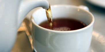 Tea being poured from a teapot into a white cup.