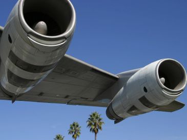 Close-up of plane engines under a wing with palm trees below.