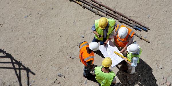 A team of construction workers huddle around a house plan, looking at it