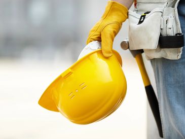 Construction worker holding a yellow hard hat and hammer.