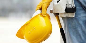 Worker holding a yellow safety helmet and tools.