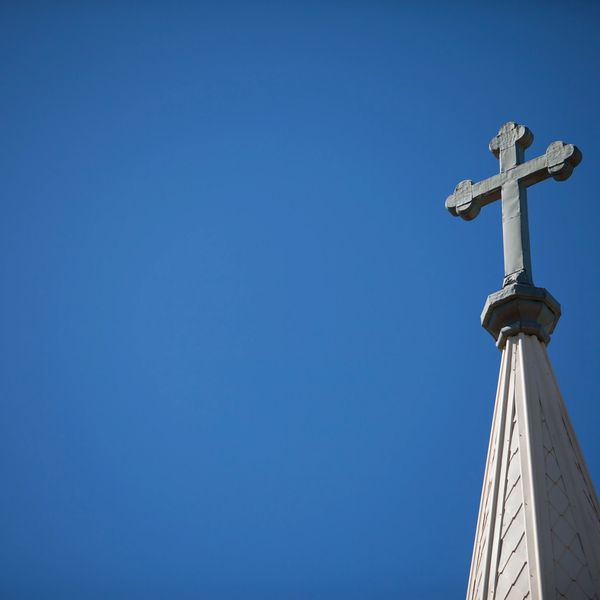 A church steeple topped with a cross against a clear blue sky.