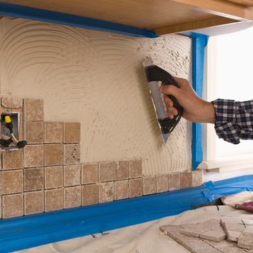 Applying adhesive to install tile backsplash in a kitchen.