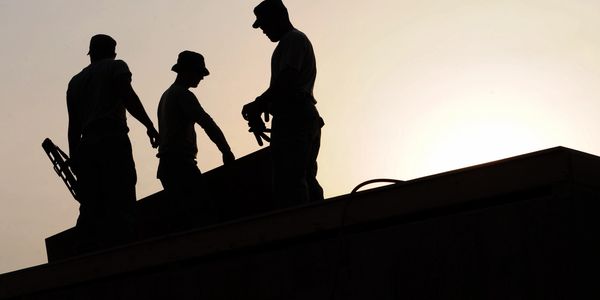 Silhouettes of three workers on a rooftop at sunset.
