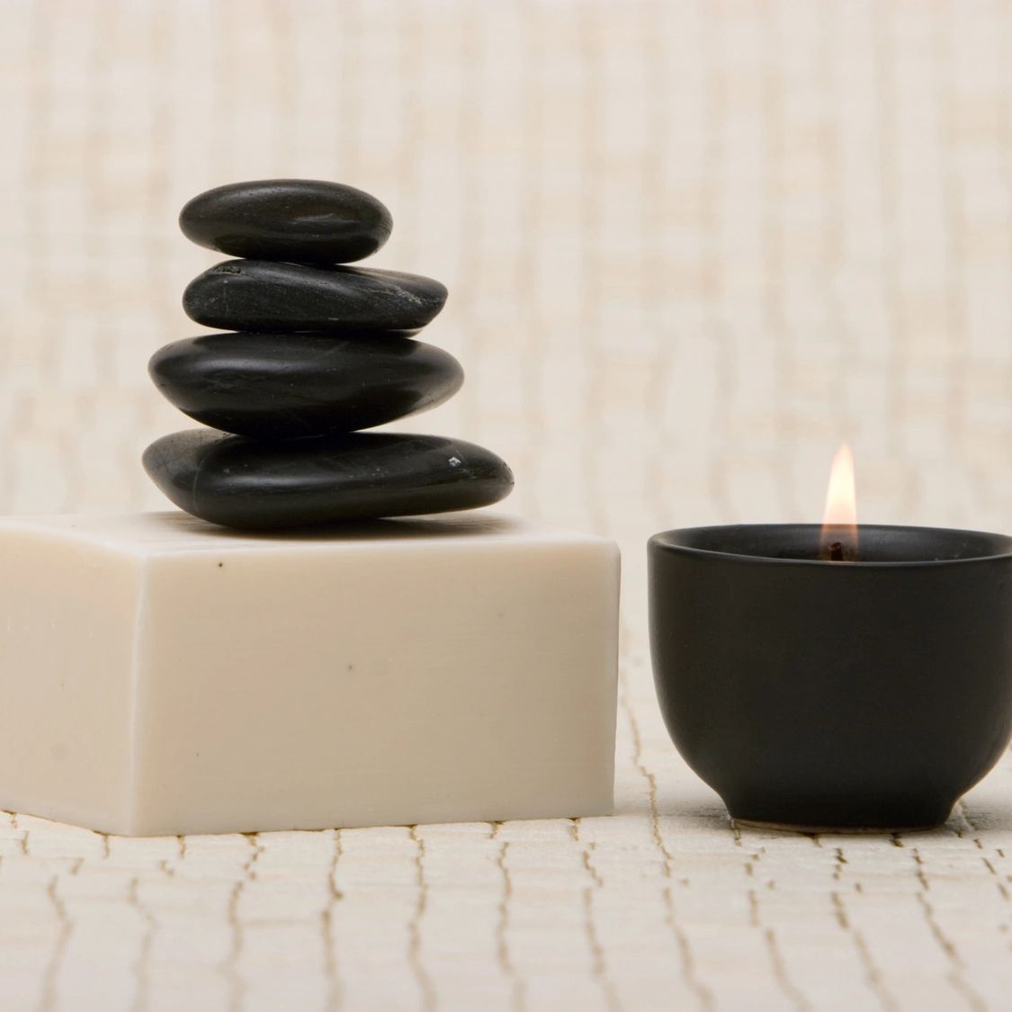 Stacked black spa stones on a white block next to a lit black candle.