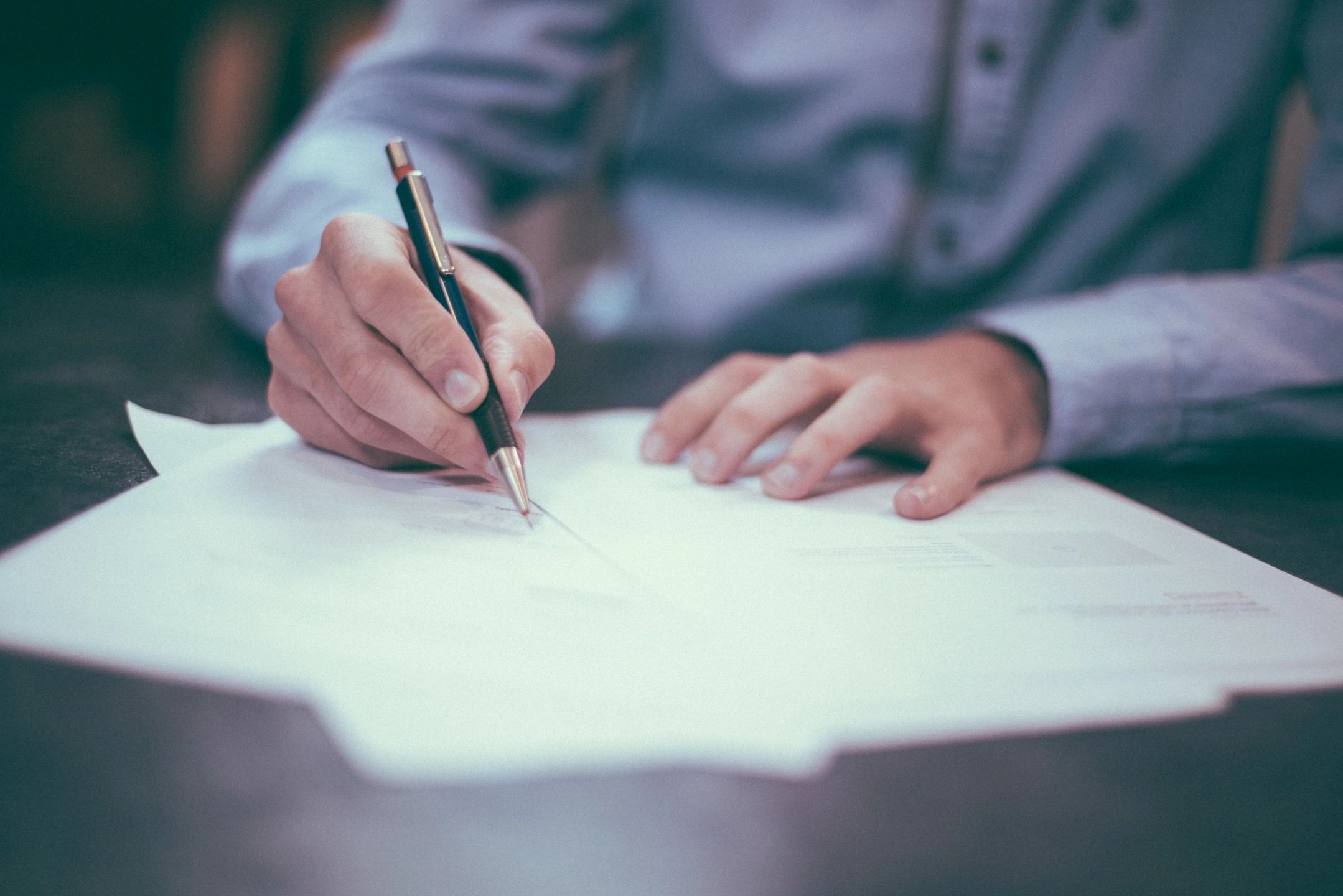 Someone signing a piece of paper with the camera focused on the hands and pen.