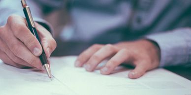 Person writing on a document with a pen.