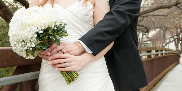 Bride and groom holding a white flower bouquet on a bridge.