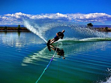 Person waterskiing on a calm lake with a vivid blue sky.