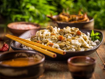 Plate of noodles with chopsticks and dipping sauces on a rustic table.