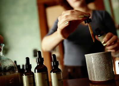 Person using a dropper to add liquid into a container, surrounded by bottles.
