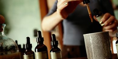 A person uses a dropper to add liquid from a tonic bottle into a ceramic cup.