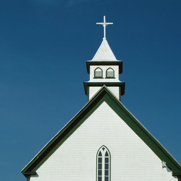 White church steeple with cross against clear blue sky.