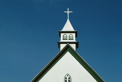 White church steeple with a cross against a blue sky.